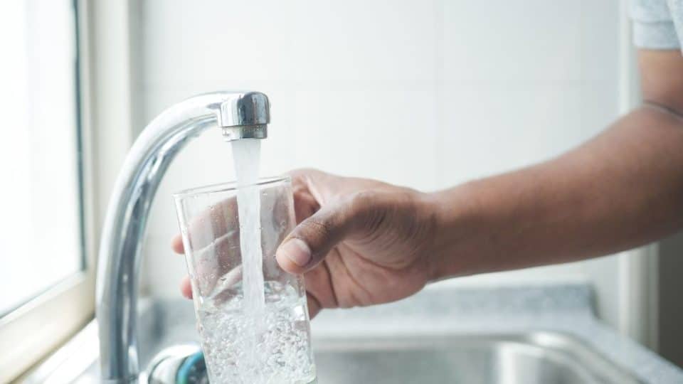 person filling a glass of water from the kitchen sink