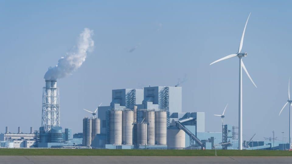 A fossil fuel power plant next to a wind mill.