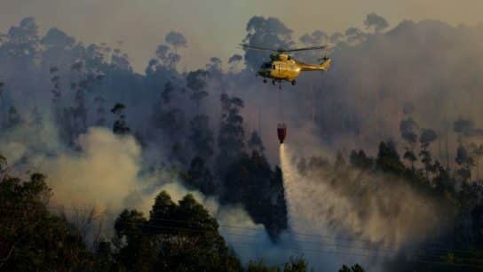 Firehawk helicopter drops water over burning forested area.