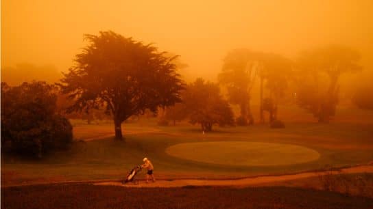 Golf player on a golf course surrounded by smoke from a wildfire.