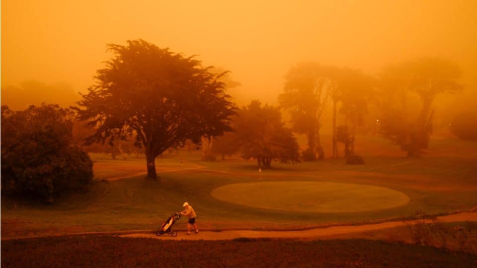 Golf player on a golf course surrounded by smoke from a wildfire.