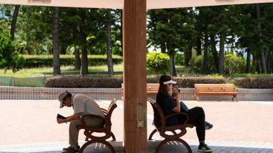 A man and woman sit on benches taking shade from the sun during a Hong Kong heatwave.