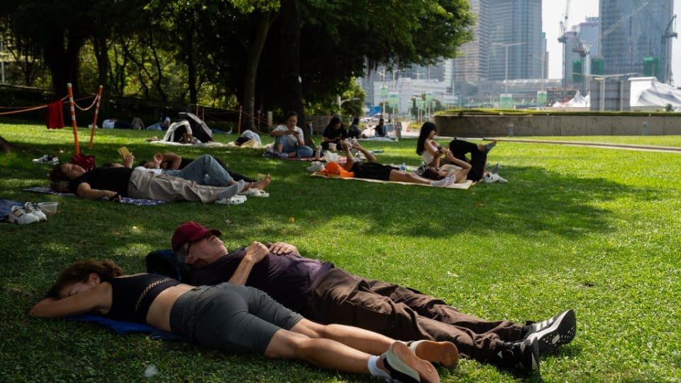 People lie on the grass under trees during a sunny heatwave in Hong Kong.